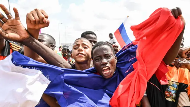 A man wrapped in a Russian flag waves his arms while supporters of Niger's military leaders gather at Niamey's French and Nigerien air bases on August 27, 2023.